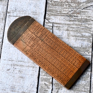 Puede incluir: Un medidor de cable de alambre de madera vintage con una parte superior de metal. El medidor presenta tablas impresas para medir el cable de alambre, incluyendo tamaño, diámetro y peso. El texto en el medidor dice "Galvanised Steel Wire Ropes" y "For All Purposes".