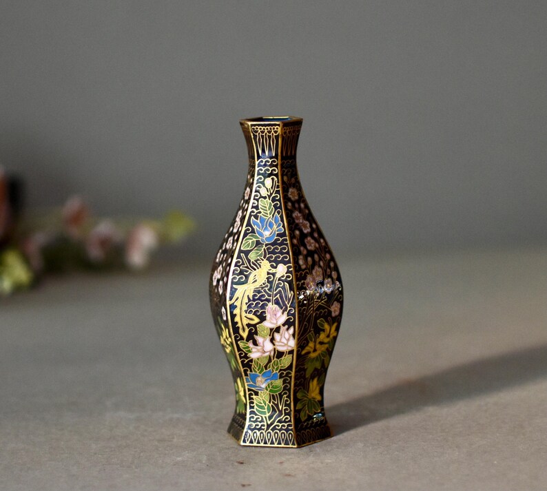 May include: A black decorative vase with a floral and bird design. The vase has a gold rim and base, with colorful flowers and birds. The vase is approximately 6 inches tall.