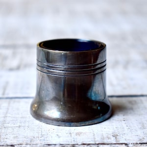 Pode incluir: Um saleiro de metal prateado com um revestimento de vidro azul. O saleiro tem um fundo arredondado e uma parte superior ligeiramente afunilada.