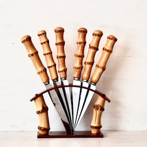 May include: Set of six stainless steel knives with bamboo handles in a brown wooden stand.