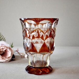 Puede incluir: Un jarrón de vidrio transparente con un patrón geométrico marrón. El jarrón tiene una boca ancha y una base redondeada.