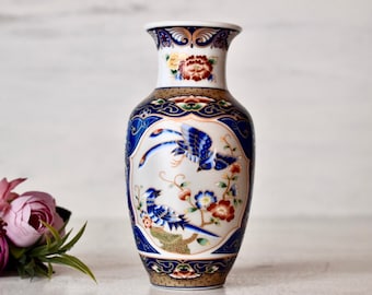 May include: A white porcelain vase with a blue and gold floral design featuring two birds. The vase has a round body and a narrow neck.