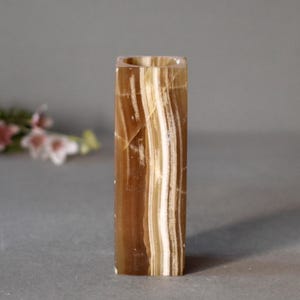 K&ouml;nnte beinhalten: Eine quadratische Onyxvase mit braunen und wei&szlig;en Streifen. Die Vase ist aus Naturstein gefertigt und hat eine glatte, polierte Oberfl&auml;che.