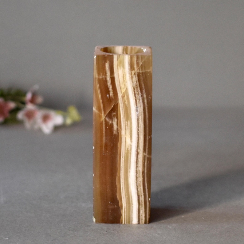 K&ouml;nnte beinhalten: Eine quadratische Onyxvase mit braunen und wei&szlig;en Streifen. Die Vase ist aus Naturstein gefertigt und hat eine glatte, polierte Oberfl&auml;che.
