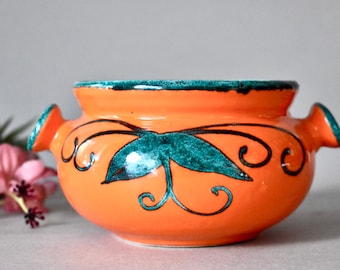 May include: Orange ceramic serving bowl with green and black floral design and two handles.