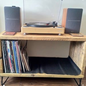 May include: A wooden record player stand with a black mesh shelf, a turntable, and two grey speakers. The stand has black hairpin legs.