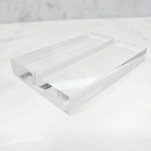 May include: A clear acrylic display stand with two slots for holding business cards or other small items.