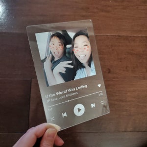 May include: A clear acrylic photo frame featuring a picture of two people in a car. The frame is designed to resemble a music player screen, with the song title "If the World Was Ending" by JP Saxe and Julia Michaels shown below the photo.