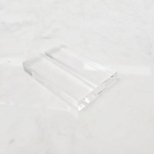 May include: A clear acrylic display stand with two slots for holding items, such as business cards or small photos.