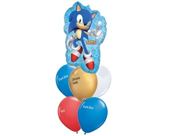 May include: A balloon bouquet featuring a large foil balloon shaped like Sonic the Hedgehog with the text Sonic the Hedgehog, accompanied by five round latex balloons in dark blue, chrome gold, white, and red colors with text labels.