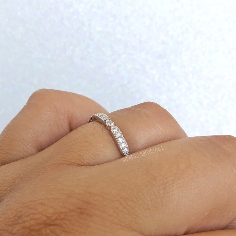 May include: A silver band ring with a row of small, clear cubic zirconia stones. The ring is on a person's finger.