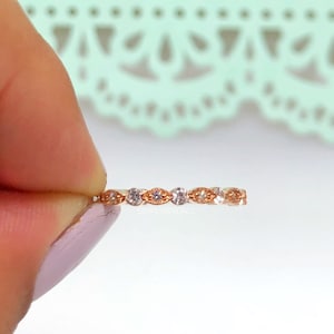 Könnte beinhalten: Ein roségoldener Bandring mit abwechselnd klaren und oval geformten Edelsteinen. Der Ring hat ein filigranes Design mit aufwendigen Details zwischen den Steinen. Der Text "SIMPLYBRIDAL" ist auf dem Ring zu sehen.