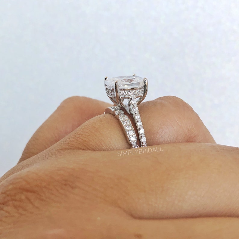 May include: A silver engagement ring set with a large oval-shaped center stone and a matching band. The ring is set with small sparkling stones.