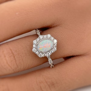May include: A silver ring with a white opal gemstone surrounded by a halo of smaller white gemstones.
