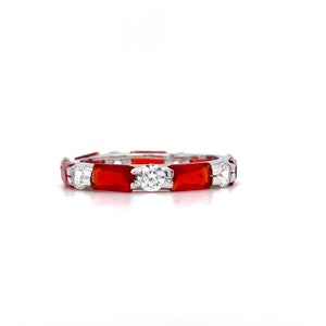 May include: A silver band ring with alternating red and clear stones. The red stones are rectangular and the clear stones are round.