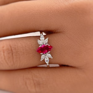 May include: A silver ring with a marquise-shaped ruby gemstone surrounded by smaller clear gemstones.
