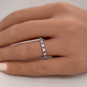 May include: A silver band ring with alternating blue and white gemstones. The ring is on a person's finger.