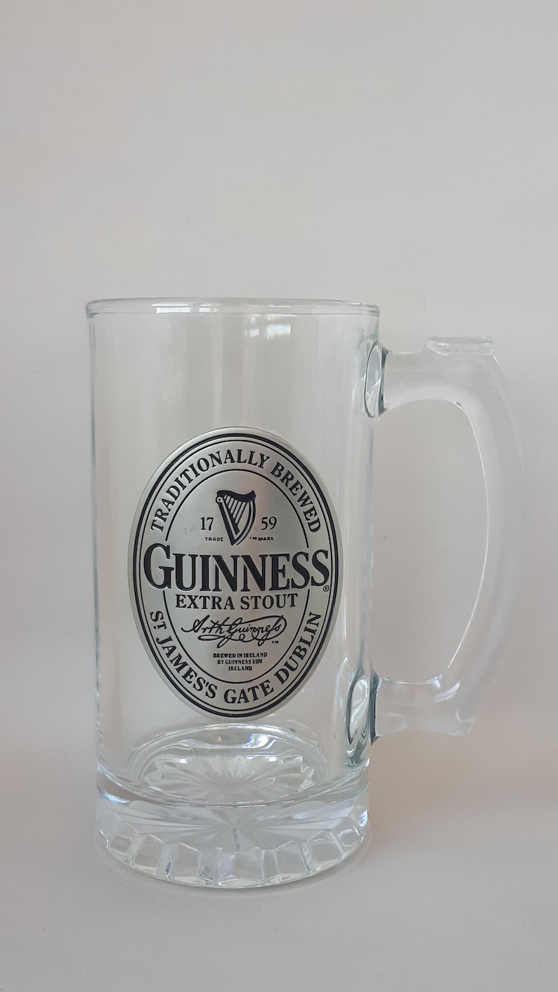 May include: A clear glass Guinness Extra Stout beer mug with a handle. The mug features the Guinness logo in black and silver, including the harp symbol and the text "St James's Gate Dublin".