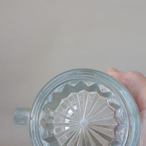 May include: Clear glass mug with a handle, featuring a starburst pattern on the base. The glass has a slightly bluish tint. The mug is designed with a rounded shape and a small handle for easy gripping.