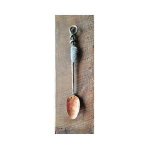 May include: A hand-forged copper spoon with a twisted metal handle. The handle is silver in color and has a loop at the top.