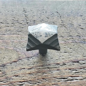 May include: A silver-toned metal cabinet knob with a diamond-shaped design. The knob has a textured surface and a slightly worn appearance.