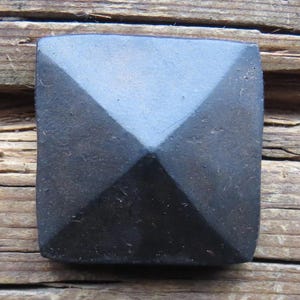 May include: A black square-shaped metal nail head with a pyramid-shaped top.