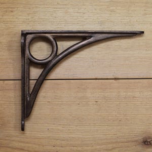 Puede incluir: Un soporte de estante de metal negro con un diseño circular decorativo. El soporte está hecho de hierro fundido y tiene un acabado rústico.