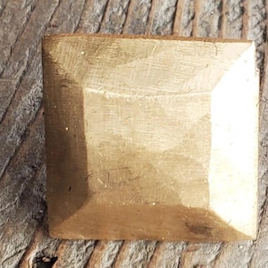 May include: A square, gold-colored metal nail head with a slightly textured surface.