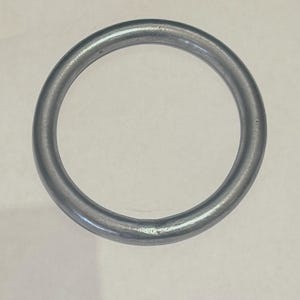 Könnte beinhalten: Ein einzelner, kreisförmiger Metallring mit mattem, silbergrauem Finish. Der Ring ist gleichmäßig geformt und scheint aus einem soliden, haltbaren Material zu bestehen. Der Hintergrund ist eine schlichte, cremefarbene Oberfläche.