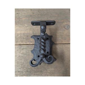 May include: Black metal door hinge with a decorative scroll design. The hinge is attached to a wooden surface.