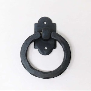 May include: Black metal ring pull handle with a decorative square backplate. The handle is designed for doors, cabinets, or drawers.