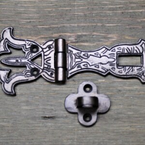 May include: A silver-toned metal latch with an ornate design. The latch has a hinge and a separate mounting plate. The latch is designed to be used on a door or cabinet.