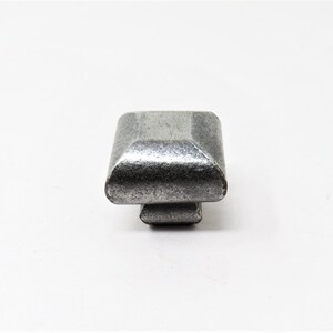 以下が含まれることがあります： わずかに盛り上がった縁とテクスチャ加工されたシルバー仕上げの正方形のキャビネットノブです。