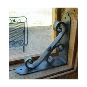 May include: A black metal shelf bracket with a decorative scroll design. The bracket is mounted to a wooden surface.