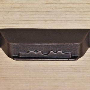 Op de afbeelding: Een donkerbruine metalen ladegreep met een decoratief, golvend ontwerp. De greep heeft een rechthoekige vorm met afgeronde hoeken.