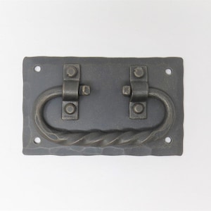 May include: A black metal drawer pull with a twisted design and two decorative hinges. The pull is rectangular and has a hammered finish.