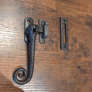 May include: A dark gray, hammered metal gate latch set featuring a long, curved handle with a decorative spiral end, a mounting plate with two screw holes, a matching catch piece, and a separate rectangular strike plate with two screw holes.