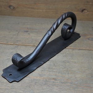 May include: A black metal door handle with a twisted design and a flat rectangular base.