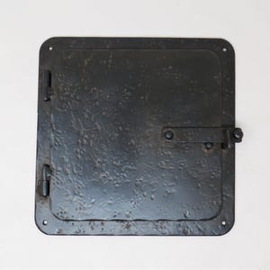 May include: A black metal door with a textured surface and a latch. The door is closed and has a rectangular shape.