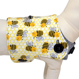 Puede incluir: Un chaleco para perro amarillo y negro con un patrón de abejas. El chaleco tiene una correa gris y un botón negro. El texto "Harness Sold Separately" es visible en la imagen.
