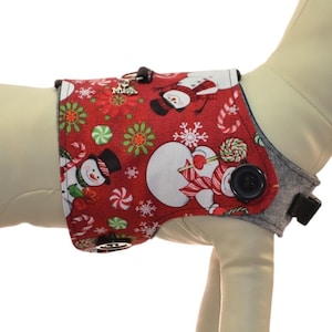 May include: A red and white dog harness with a snowman pattern. The harness has a button closure and is shown on a dog mannequin. A size chart is included with neck, chest, and weight measurements in inches and pounds.