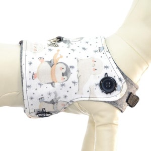 May include: White dog vest with a penguin and polar bear print. The vest has a gray trim and a button closure. "Harness Sold Separately See Description for Details" is written on the image. "It's a doggy thing Pawzly.com" is written on a green circle with a reindeer.