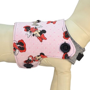 May include: Pink dog harness cover with a Minnie Mouse print. The harness cover features a button closure and is shown on a small dog mannequin. "Harness Sold Separately See Description for Details" and "Size Small Harness/Cover Featured" are printed on the image.