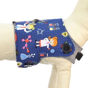 May include: Blue dog vest with a science theme featuring a girl scientist, beakers, and molecules. The text "Harness Sold Separately See Description for Details" is visible in the image.