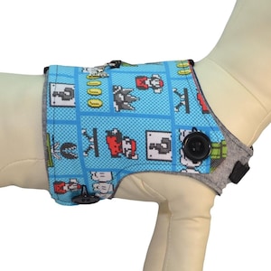 May include: A blue dog vest with a pixelated video game design. The vest has a gray adjustable strap and a black button. "Harness Sold Separately See Description for Details" is written in black text on a white background.