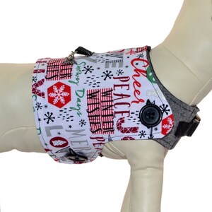May include: A white dog harness with a red and white Christmas print featuring the words "Peace", "Cheer", "Merry Days", and "Love". The harness has a grey adjustable strap and a black button. A size chart is included in the image.