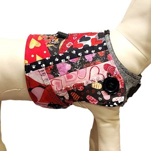 Puede incluir: Un arnés para perro rojo, rosa y negro con un patrón de corazón y un botón negro. El arnés está en un maniquí blanco.