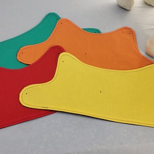Puede incluir: Cuatro formas de tela en diferentes colores: verde, naranja, rojo y amarillo. Las formas están recortadas en fieltro y tienen un contorno negro. Están dispuestas en una pila, con la forma verde en la parte superior y la forma amarilla en la parte inferior.
