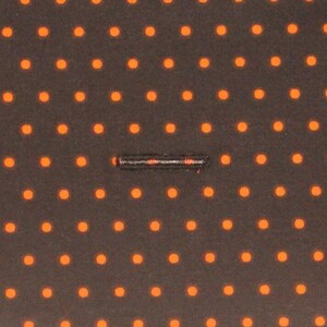 May include: A close-up of a black fabric with a repeating pattern of small orange dots. A thin black line runs horizontally across the center of the fabric.