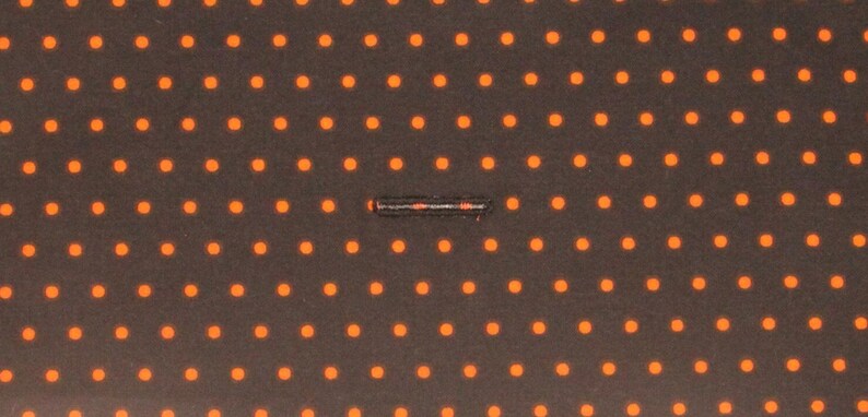 May include: A close-up of a black fabric with a repeating pattern of small orange dots. A thin black line runs horizontally across the center of the fabric.